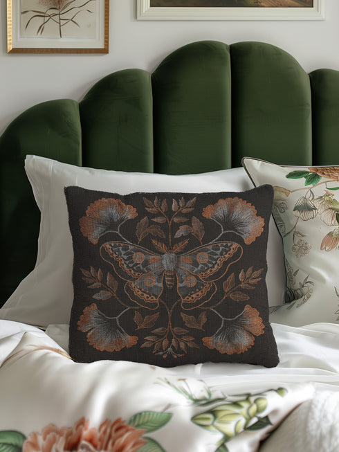 A square decorative pillow featuring an intricately detailed Luna moth in copper, terra cotta and slate blue colors on a black background. The moth is centered in a symmetrical arrangement with ginkgo-inspired leaves and botanical elements surrounding it.
